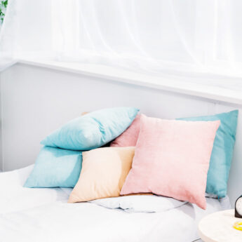 comfy bed with lot of pillows in modern light room with alarm clock and plant of bedside table